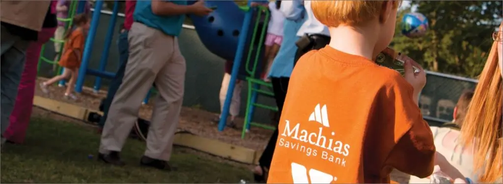 a young child with an orange Machias Bank shirt on, in a playground