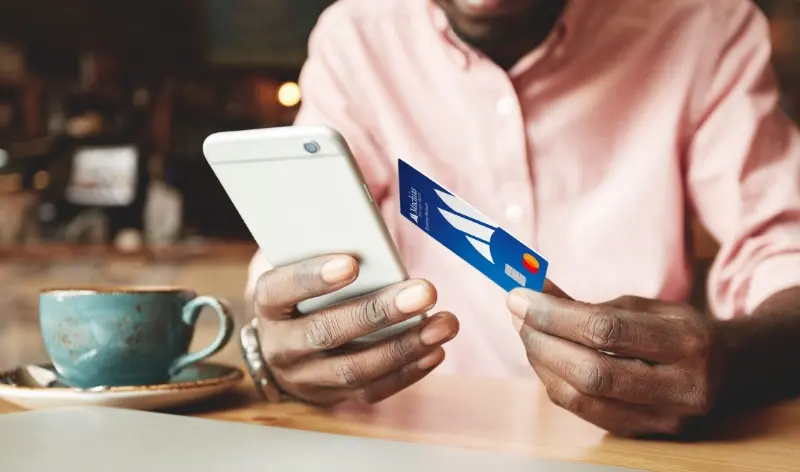 a person holding a credit card with one hand, next to their phone in the other hand