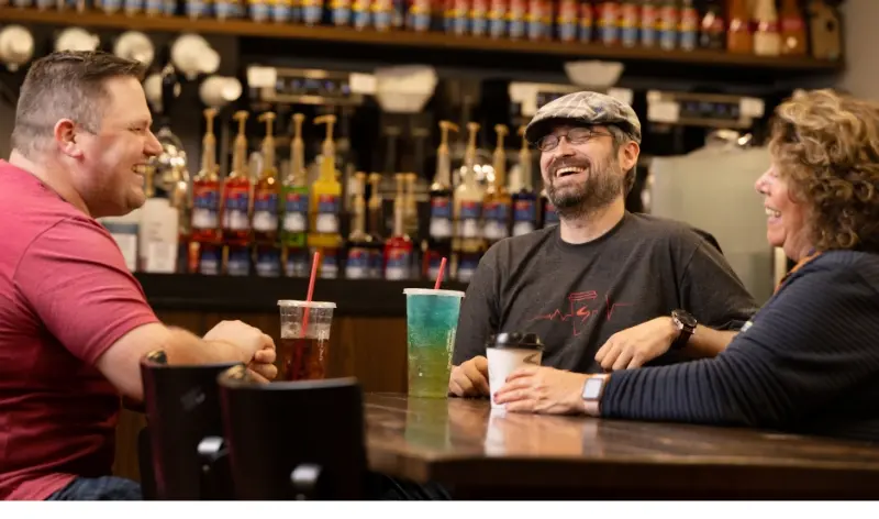 three people at a café, sitting at a table laughing