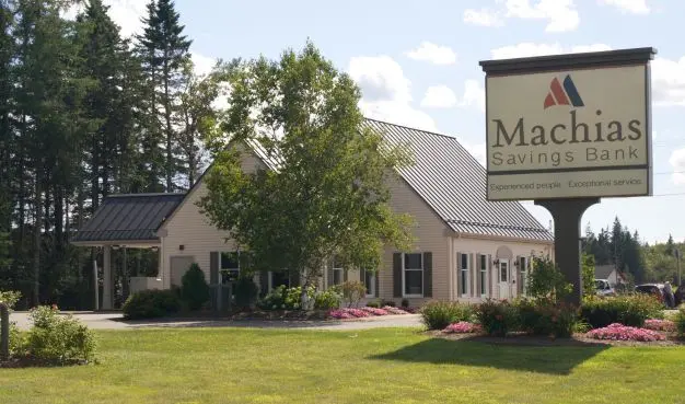 a salmon colored building, with a large sign next to it that says "Machias Savings Bank"