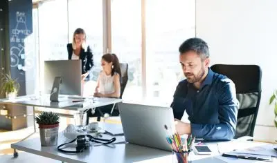 a man working at a computer in an office, with two people in the background