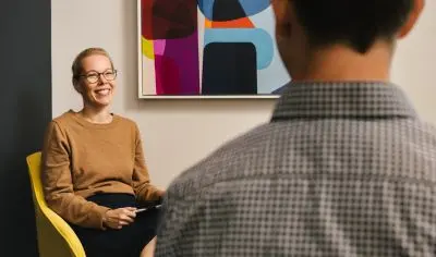 a woman sitting in a yellow chair, smiling at a person in front of them