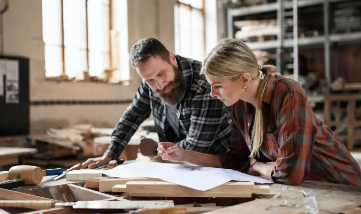 man and woman looking at sheet of paper in woodshop