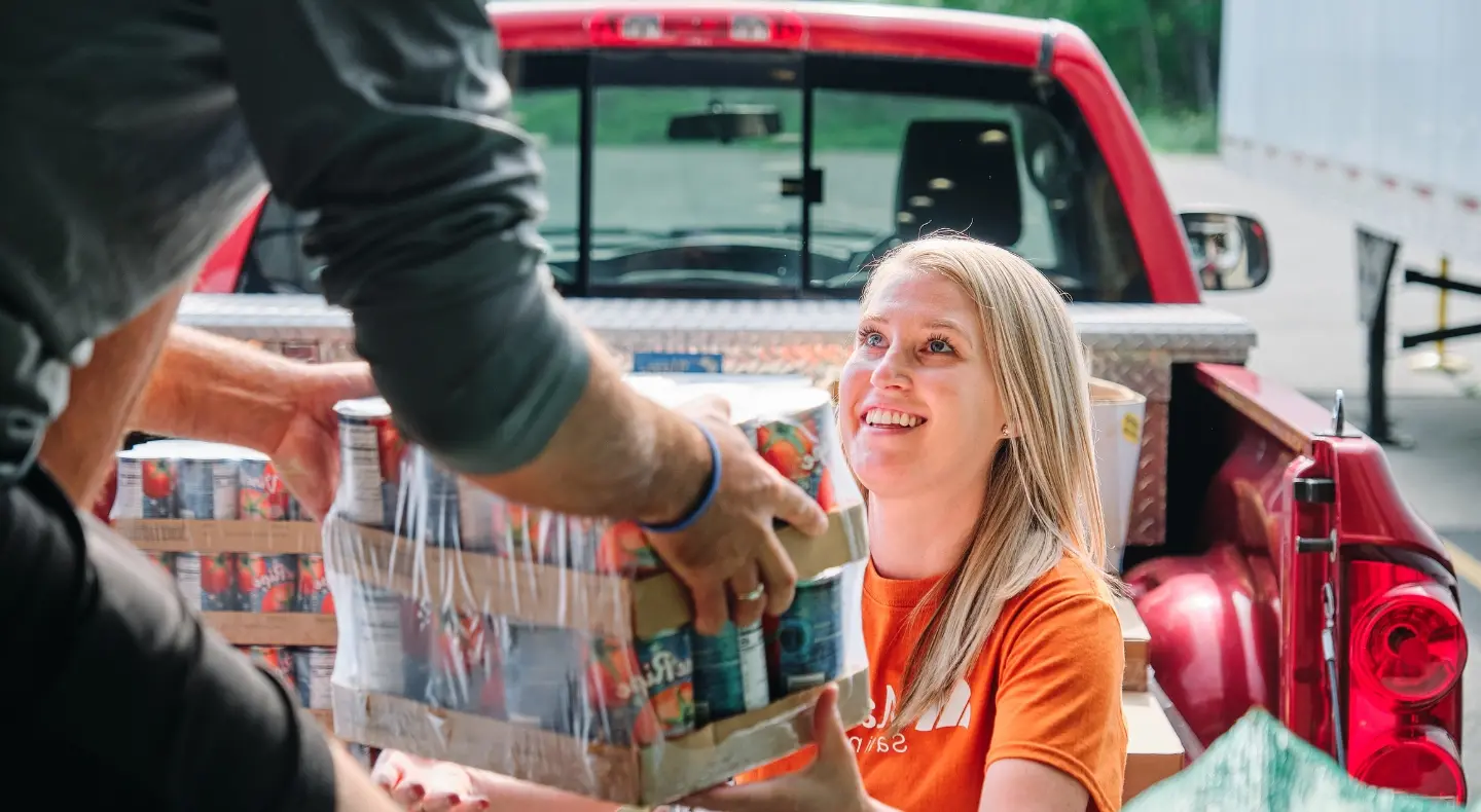 smiling woman being handed a box of cans with tomatoes on them