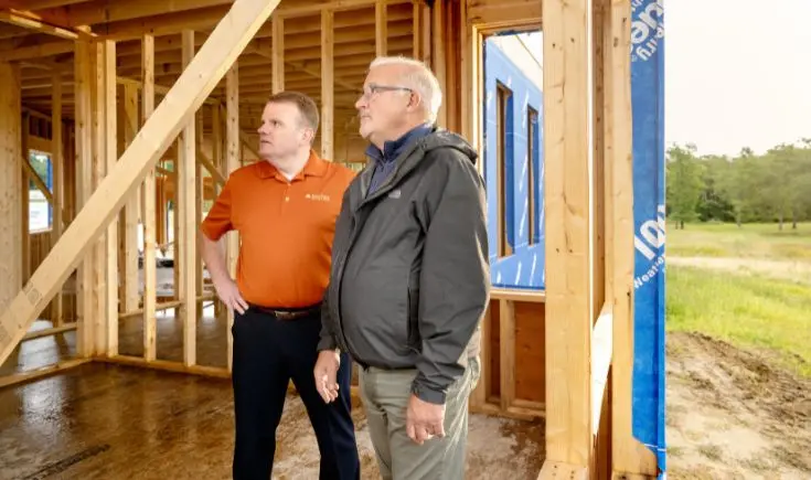 two men standing next to another looking at construction of house