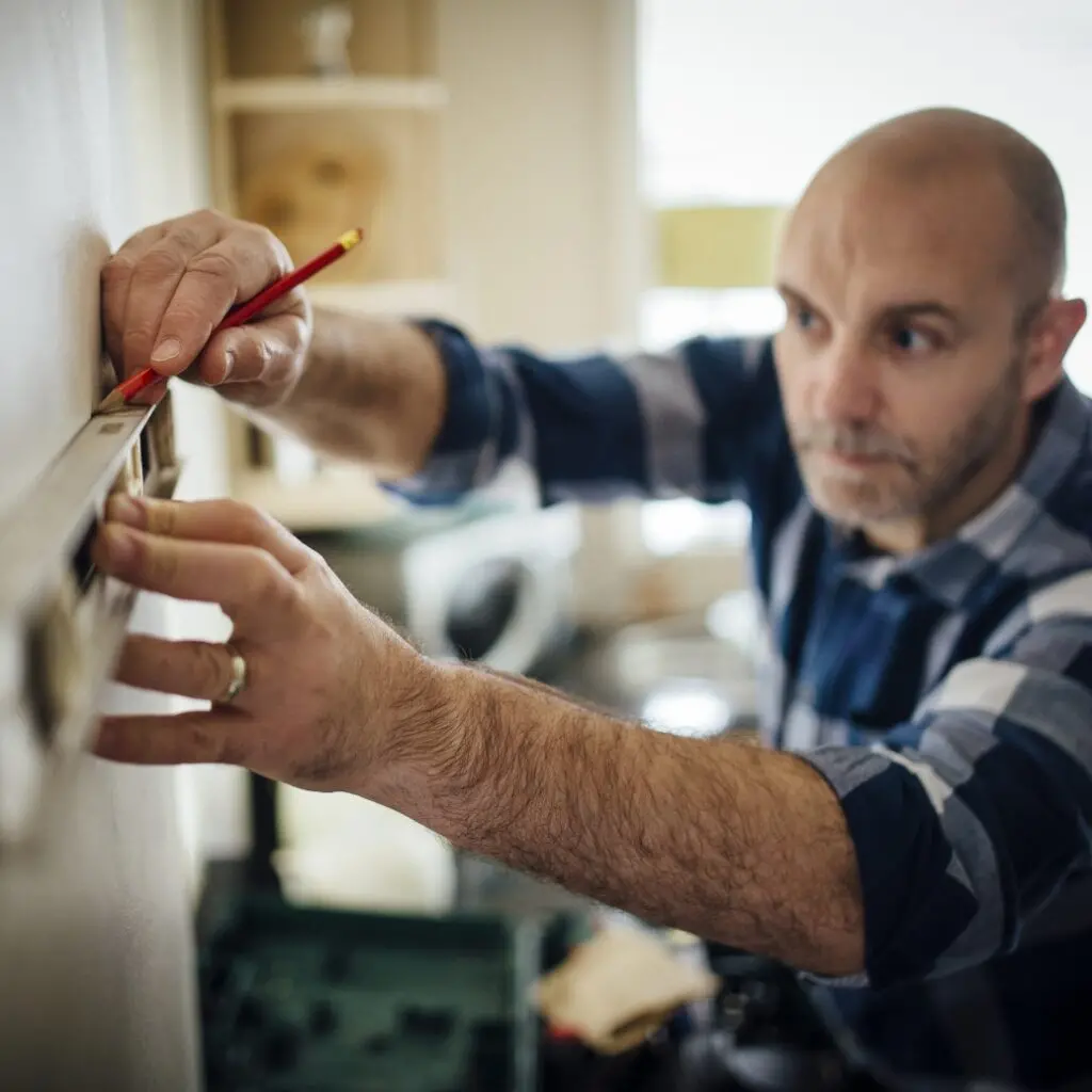 a man using a straightedge tool, measuring a section of a wall