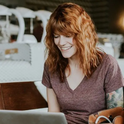 a person smiling at their computer screen while sitting down