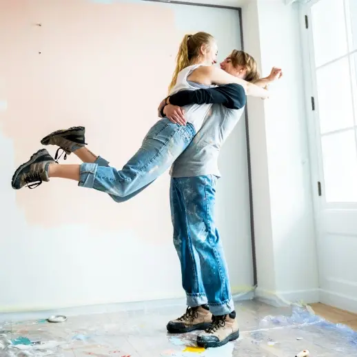 a happy couple embracing, with paint stains on their clothes, in a room with half painted walls
