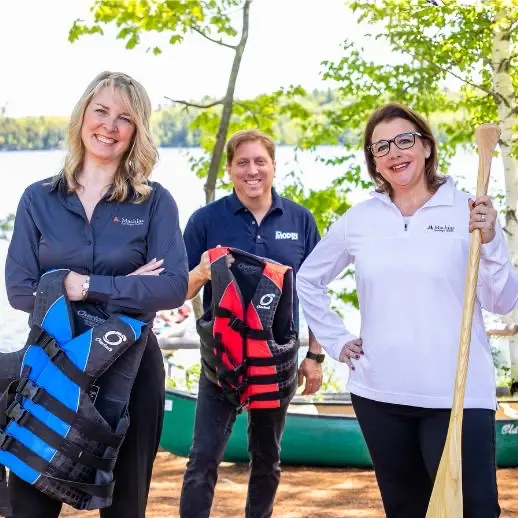 Three people holding life vests and canoe paddle