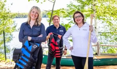 Three people holding life vests and canoe paddle