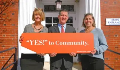three people holding an orange sign that says "yes! to community"