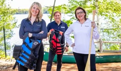 Three people holding life vests and canoe paddle