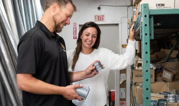 man and woman smiling and looking at piece of metal