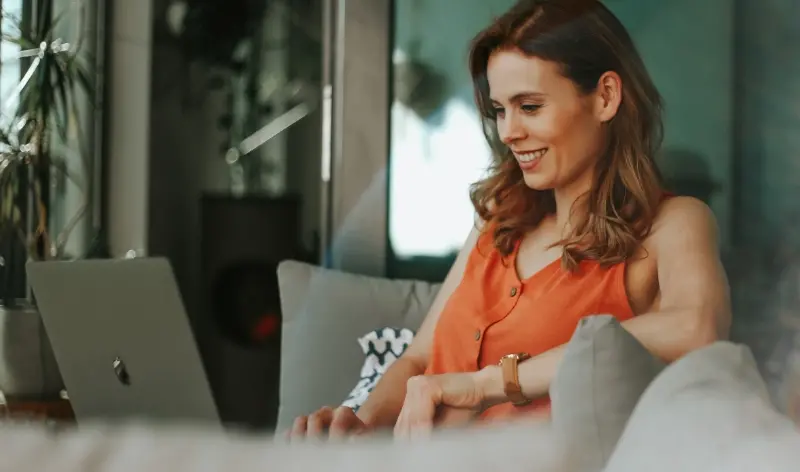 a woman in an orange shirt, smiling at a computer