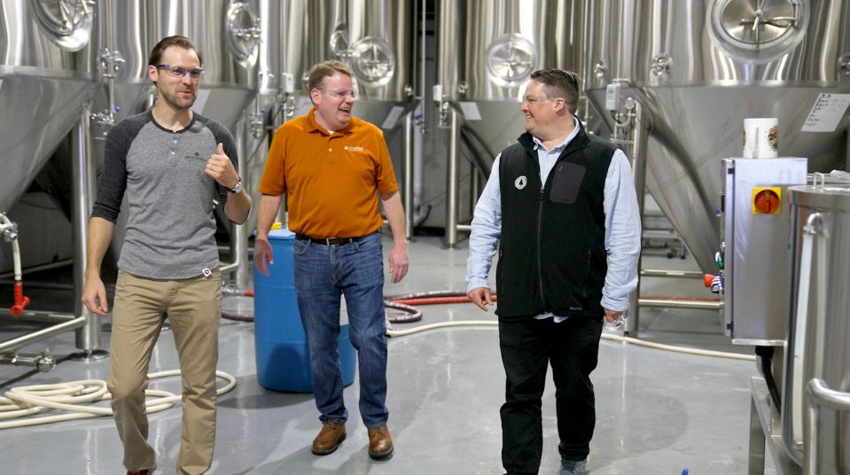 three men with safety glasses walking through a brewery