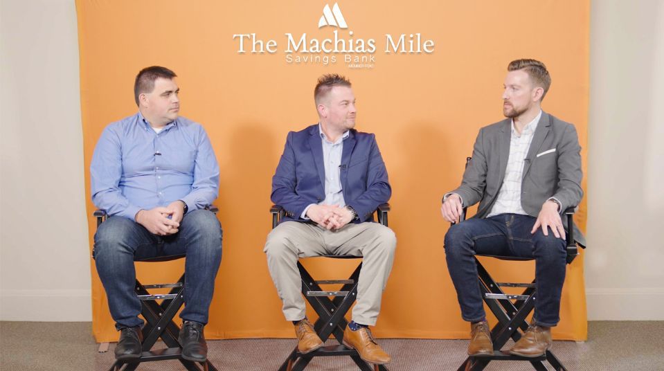 Three men in front of Machias Mile orange background