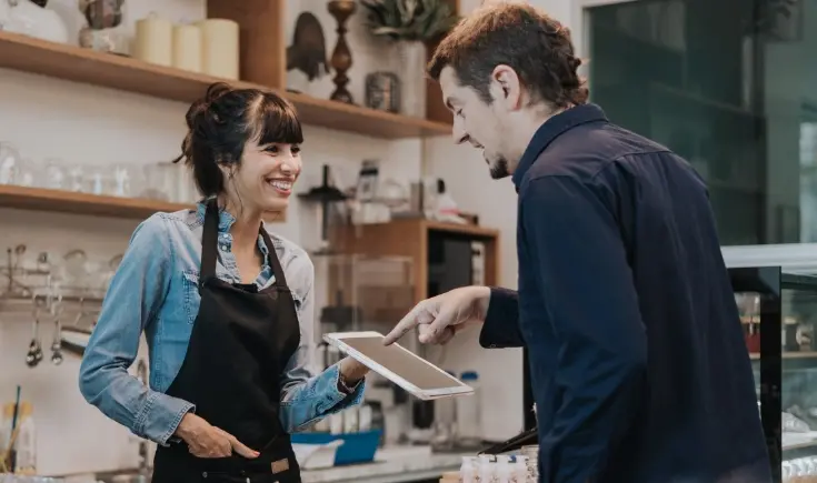 a café employee holding up a touchscreen device to a man, who is pointing at it