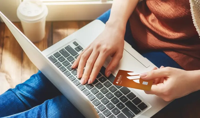 person holding Machias Bank credit card while typing on a computer