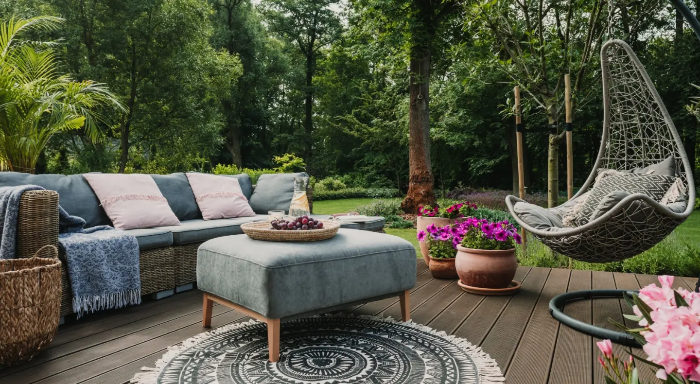 an outside deck with a green hammock chair, a blue couch and greenery all around