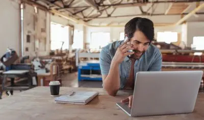 a man on the phone, sitting at a computer, in a building