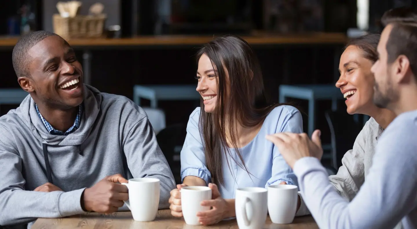 a group of people chatting and laughing, while holding coffee cups