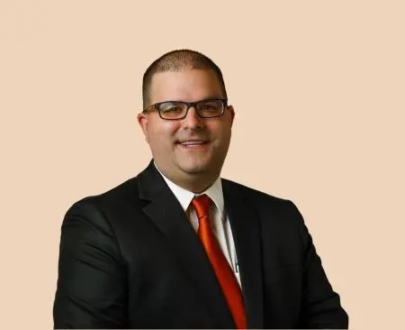 man smiling wearing black suit jacket over white button-up shirt with orange tie