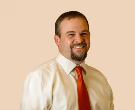 man smiling wearing white button-up shirt with orange tie