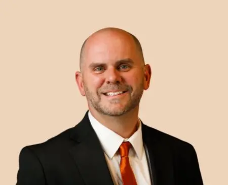 smiling man in black suit jacket with orange tie