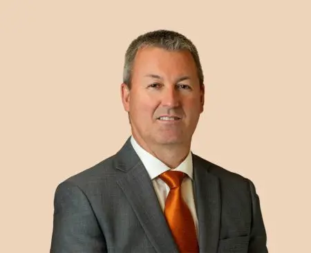 man smiling wearing gray suit jacket, white button-up shirt, and orange tie