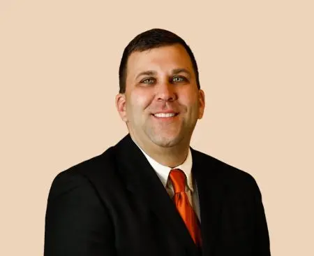 man smiling wearing suit jacket, white button-up shirt, and orange tie