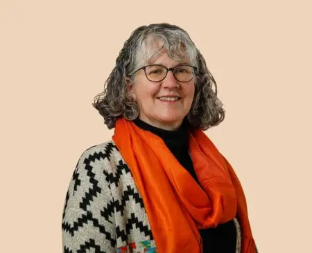 woman smiling wearing a patterned gray and black cardigan over a black top with an orange scarf