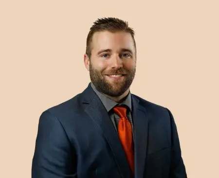 man smiling wearing navy suit jacket over gray button-up shirt with orange tie