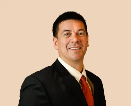 man smiling wearing black suit jacket over white button-up shirt with orange tie