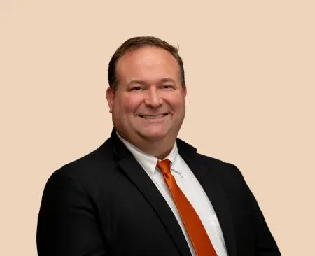 man smiling wearing black suit jacket over a white button-up shirt with orange tie