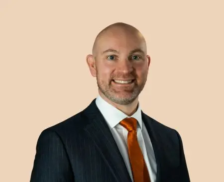 man smiling wearing black suit jacket over white button-up shirt with orange tie