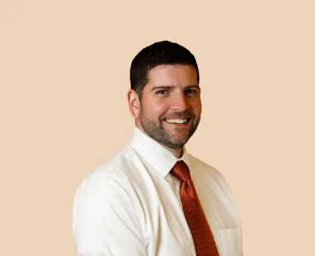 man smiling wearing white button-up shirt with orange tie