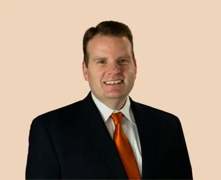 man smiling wearing black suit jacket over white button-up shirt with orange tie