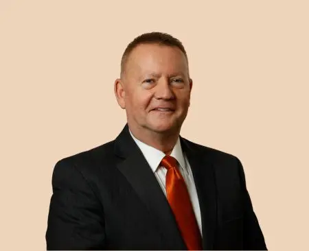 man smiling wearing black suit jacket over white button-up shirt with orange tie