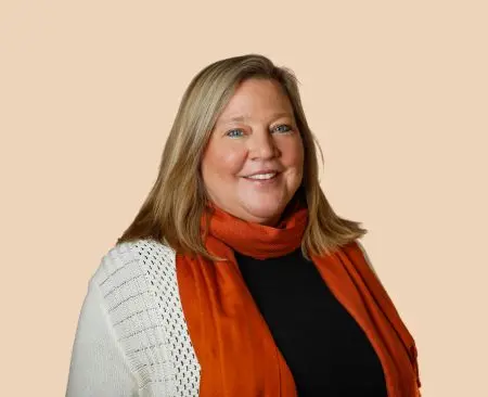 woman smiling wearing a white cardigan over a black top with an orange scarf