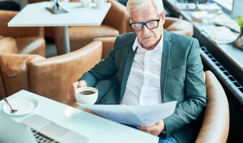 gentleman sitting in chair reading paper holding a cup of coffee