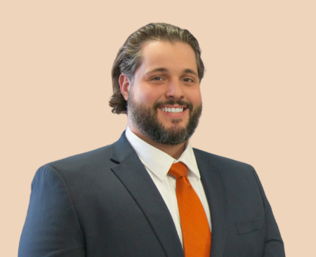 Man, smiling wearing navy blazer, white button up and orange tie